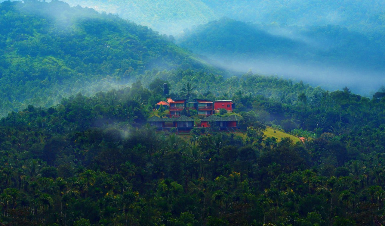 The inn's red-roofed cottages seen across a misty valley in the Western Ghats